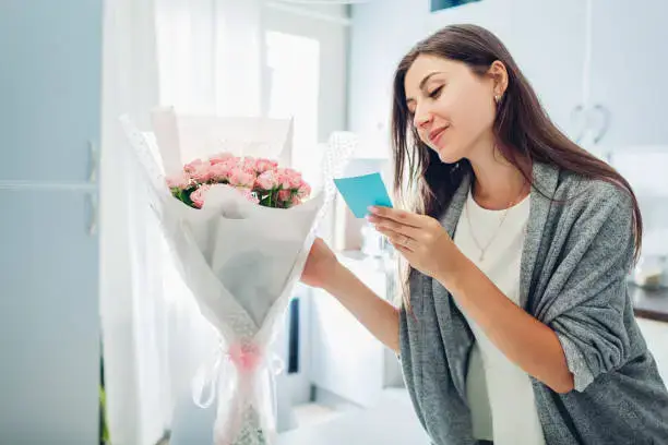 Smiling woman reading a card with pink flower bouquet at home from a flower shop Dubai