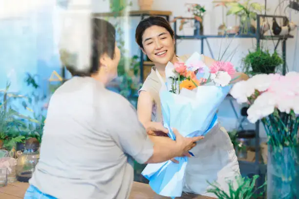 Elegant woman offering a flower bouquet to an older lady at a flower shop in the UAE.