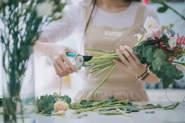 Florist trimming flower stems while arranging bouquet at flower shop in Umm Al Quwain