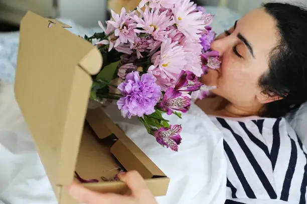 Woman receiving fresh flowers in a box, bouquet from AED 100 at Flowersmart.ae, same-day delivery in UAE.